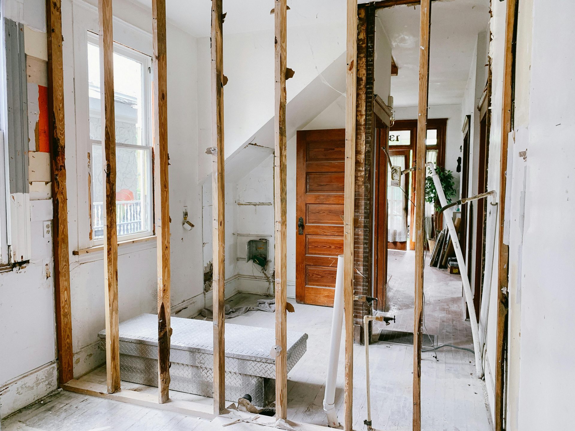 Vue intérieure d'une maison en rénovation avec poutres et porte en bois apparentes.