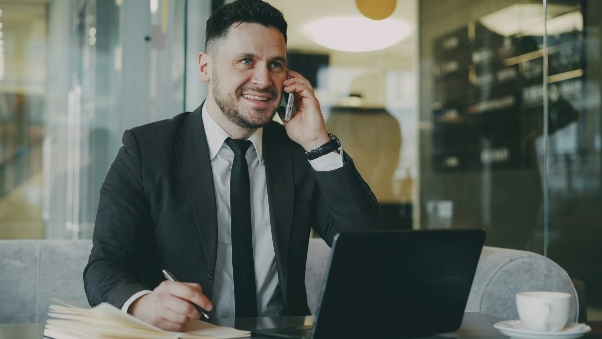 Un homme en costume parle au téléphone avec son ordinateur portable.